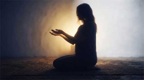 Silueta femenina serena con manos en gesto de ofrenda ante luz dorada suave, atmósfera de compasión silenciosa y entrega espiritual