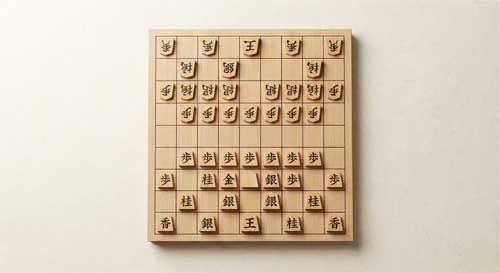 Tablero de Shogi con piezas pentagonales de madera dispuestas en formación, mostrando la densidad del juego
