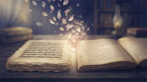Composición contemplativa en tonos índigo, beige pergamino y dorado suave: dos manuscritos antiguos abiertos lado a lado sobre escritorio de madera, uno con escritura devanagari sánscrita y otro con notas de traducción en español; encima flotan pétalos de loto translúcidos que se disuelven en partículas de luz al tocar el espacio entre textos; resplandor dorado brota del intersticio entre ambos manuscritos