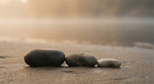 Tres piedras lisas alineadas sobre arena húmeda simbolizando las Tres Joyas como orientación interior