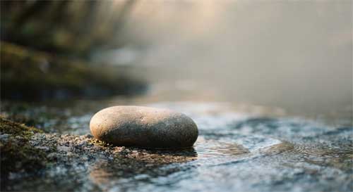 Piedra junto a arroyo donde el agua fluye alrededor sin resistencia simbolizando adaptación sabia