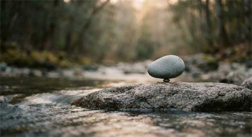 Piedra equilibrada sobre roca junto al agua simbolizando esfuerzo correcto sin tensión ni apego