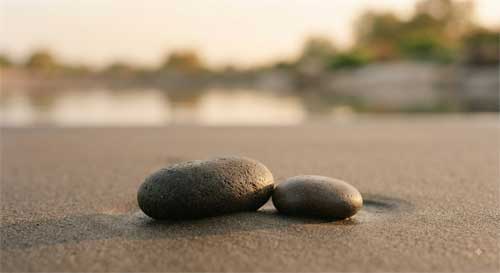 Dos piedras lisas sobre arena húmeda al amanecer simbolizando presencia compasiva sin apego emocional