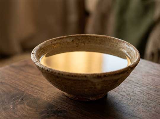 Un cuenco sencillo con agua tranquila reflejando una luz suave