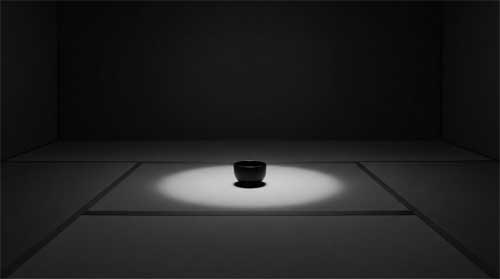 Sala de té oscura y minimalista con tatami gris carbón, cuenco negro mate colocado con precisión milimétrica en centro geométrico, luz tenue cenital creando halo circular perfecto alrededor del objeto, atmósfera de silencio absoluto y concentración extrema