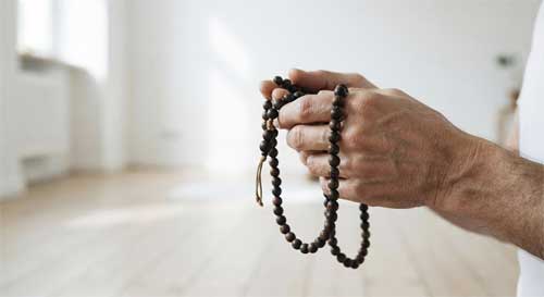 Primer plano de manos sosteniendo un mala de cuentas antiguas, con un fondo desenfocado de una sala de meditación minimalista y luminosa