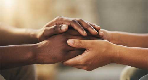 Dos manos entrelazadas suavemente, una sosteniendo a la otra con delicadeza, simbolizando el apoyo compasivo y la conexión humana
