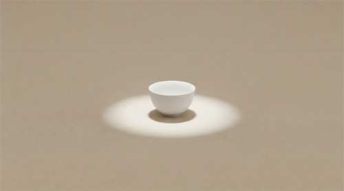 Composición extremadamente minimalista: cuenco de té blanco puro colocado exactamente en centro geométrico sobre tatami beige uniforme, sin ningún otro objeto visible en encuadre, iluminación cenital difusa creando sombra circular perfecta debajo