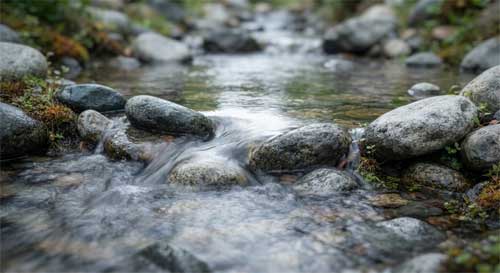 Agua fluyendo suavemente alrededor de piedras lisas en un arroyo, adaptándose perfectamente a cada obstáculo sin resistencia ni esfuerzo