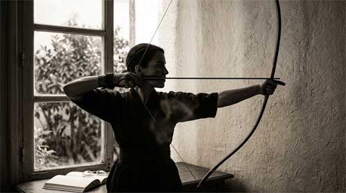 Arquero de Kyudo en postura formal con arco yumi largo contra un fondo minimalista