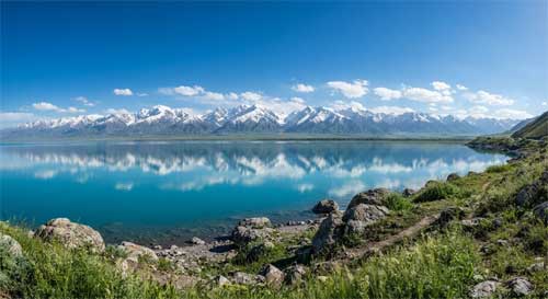 Vista panorámica del lago Sayram en Bortala, aguas cristalinas azul turquesa reflejando picos nevados de las montañas Tian Shan bajo un cielo despejado