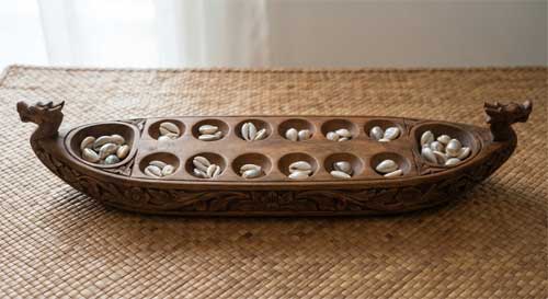 Tablero de Congkak de madera tallada con forma de barcaza, lleno de conchas marinas brillantes