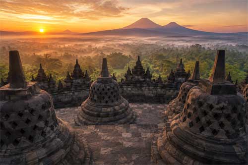 Vista aérea del templo de Borobudur al amanecer con stupas perforadas y volcanes de fondo