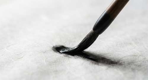 Primer plano de un pincel de caligrafía china depositando tinta negra sobre papel de arroz, mostrando la fluidez y el contraste entre lo lleno y lo vacío