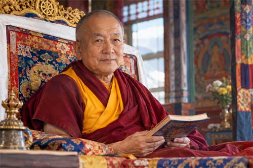 Thrangu Rinpoche sentado en trono ceremonial con vestimenta monástica roja, sosteniendo un texto budista y con una expresión de profunda calma y sabiduría