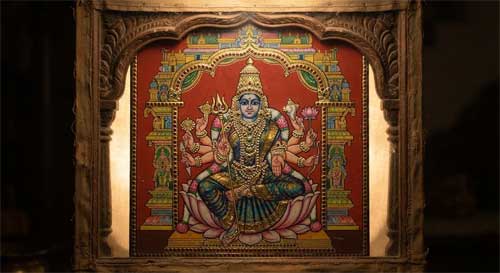 Pintura tradicional india sobre vidrio reverse-painting, diosa hindú frontal con múltiples brazos, fondo rojo intenso, detalles dorados brillantes simulando joyas